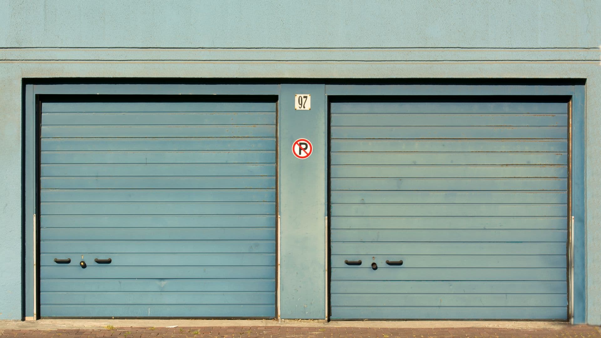 A garage door technician kneeling beside a torsion spring on a residential garage door, tools laid out, morning light