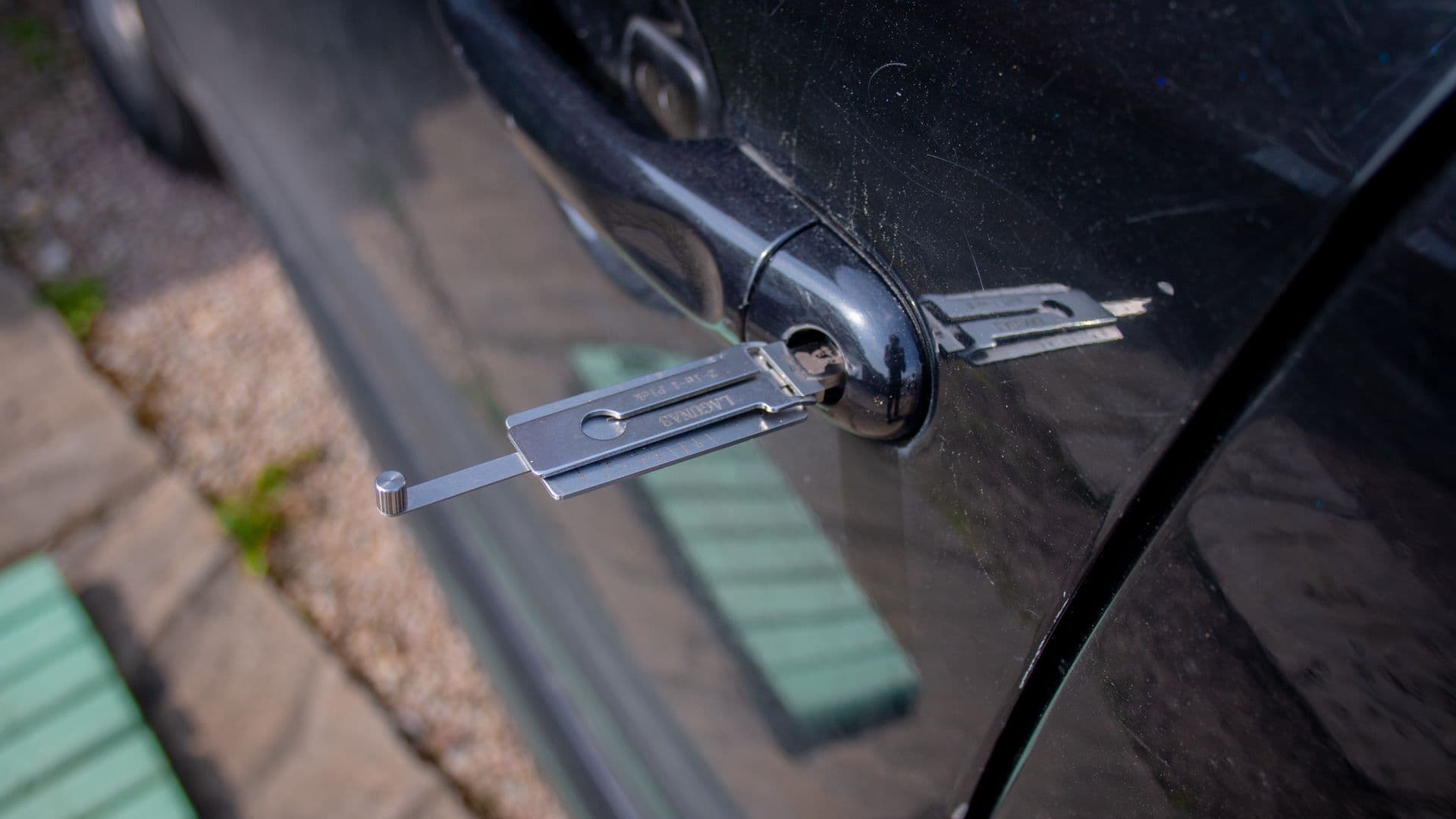 A locksmith working on a car door lock at night under street light, tools and a work light visible